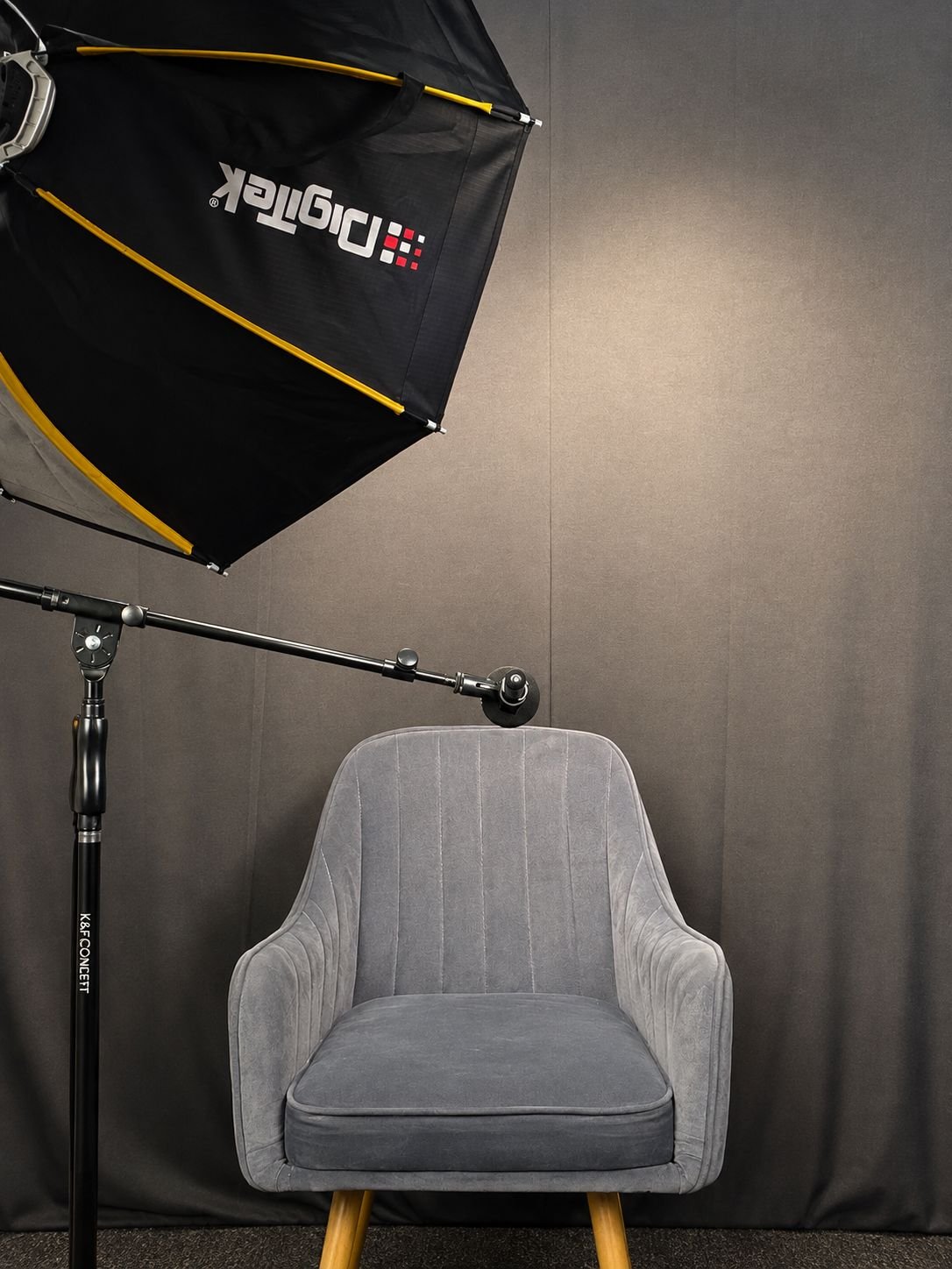 A grey armchair in the podcast studio under a large softbox light on a stand, in front of a dark backdrop.